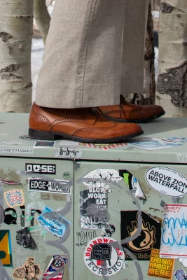 A pair of brown leather loafers stands atop a pale green power box covered in stickers.