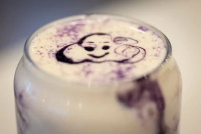 A close up shot of an Ube latte that has an syrup image of a cloud smiling drizzled on it. 