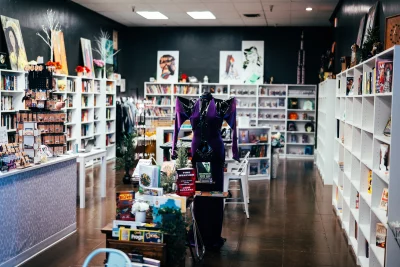 Interior shot of Mosaics Community Bookstore & Venue. White shelves line the walls with multicolored books. A purple costume in the center of the room on display.