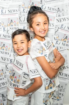 Mei and Ren stand in front of a wall covered in the front pages of Kid News. 