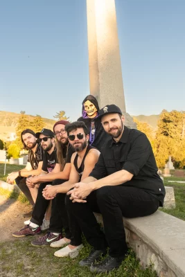 The members of Sean Baker's Recycled Stardust sit on a bench in a line together. 