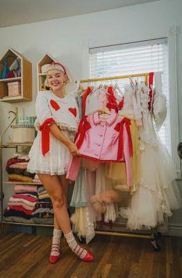 Zander cheekily smiles and holds up a pink and red frilly blazer from her clothing rack.