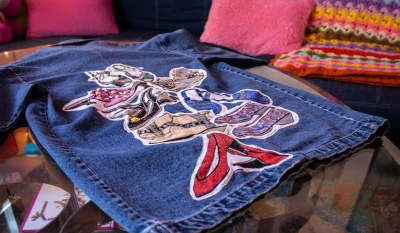 A denim jacket with a shoe pattern embroidered on it rests on a coffee table.