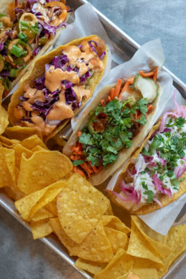 Four tacos on a tray with chips. 