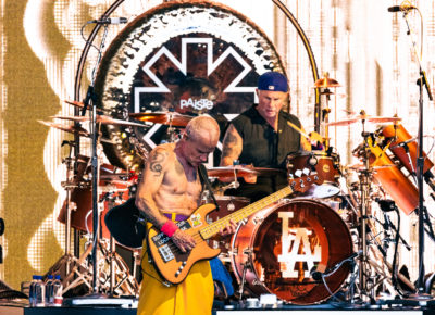 Bassist Flea of the Red Hot Chili Peppers sports a shirtless look with a yellow fabric skirt as he plays with drummer Chad Smith right behind him in Salt Lake City, Utah. Photo: @lmsorenson