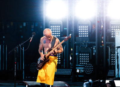 Flea, bassist for the Red Hot Chili Peppers, plays in front of a blast of white light from the stage as he is in the zone, looking down at his instrument. Photo: @lmsorenson