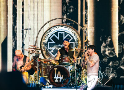 Flea plays bass, Chad Smith plays drums while shouting a lyric and Anthony Kiedis sings with mic in hand while on stage in Salt Lake City, Utah. Photo: @lmsorenson