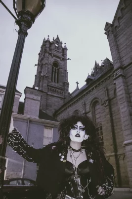 Cherry Poppins leans against a lightpost in front of a cathedral.