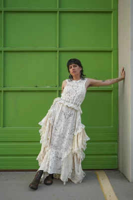 Regan Ku'ulei poses in a white lace dress against a bright green wall. 