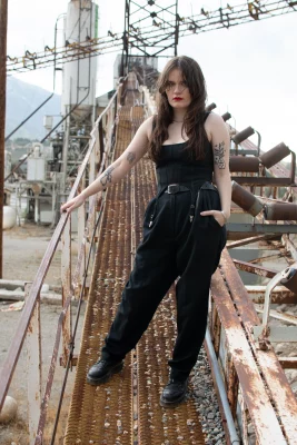 Ophelia May, Mercy Seat, stands atop a rusty metal catwalk. The background looks to be an abandoned construction site. 