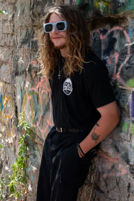 Zach Anderson, Balduvian Bears, stands in front of a rocky graffiti covered wall. His hands in his pockets.