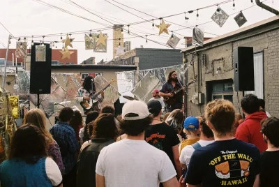 A crowd looks on as the band, Little Barefoot, plays on an outdoor stage. Decorations of stars and flags hanging above their heads. 