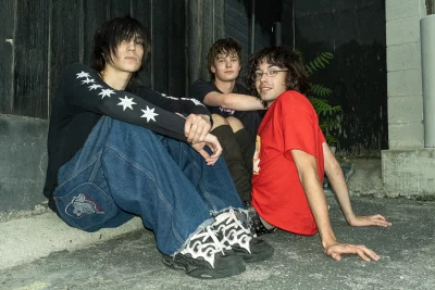 The members of eardrums sit on concrete in an alley.