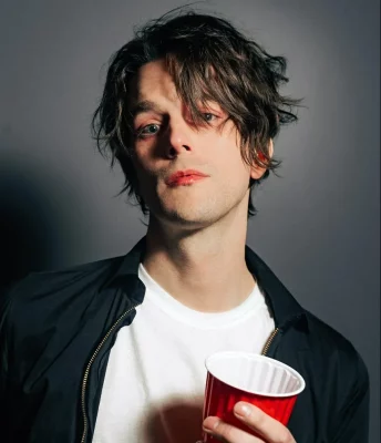 Photo Weekes in front of a gray background. He looks into the camera holding a red solo cup.