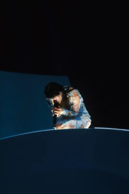 Maria of the Maria's sings into a microphone while kneeling on stage.