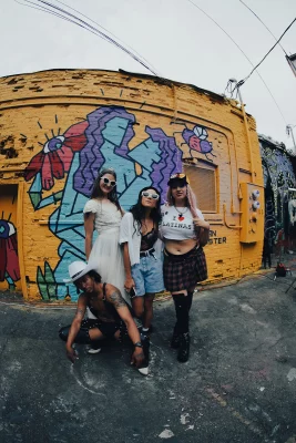 Four women stand in front of a yellow wall with a mural of two women embracing.