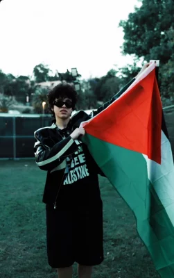 Person standing in field holding up a Palestine flag.