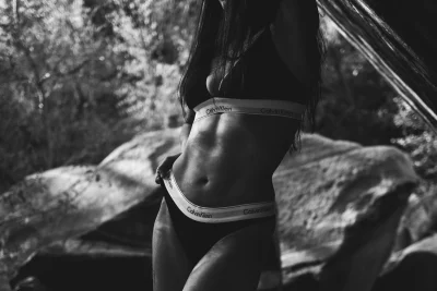 Black and white image of a woman's body in Calvin Klein lingerie. A rocky background behind it.