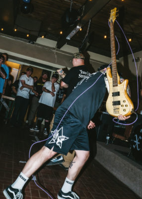 A man swings his bass guitar while playing a show.