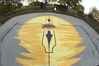 A mural of a yellow circular object and an eye on a concrete soccer court.