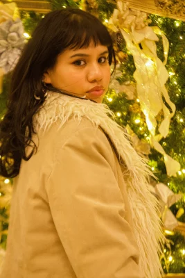 Aura Martinez Sandoval looks back at the camera in front of a lit Christmas tree. 